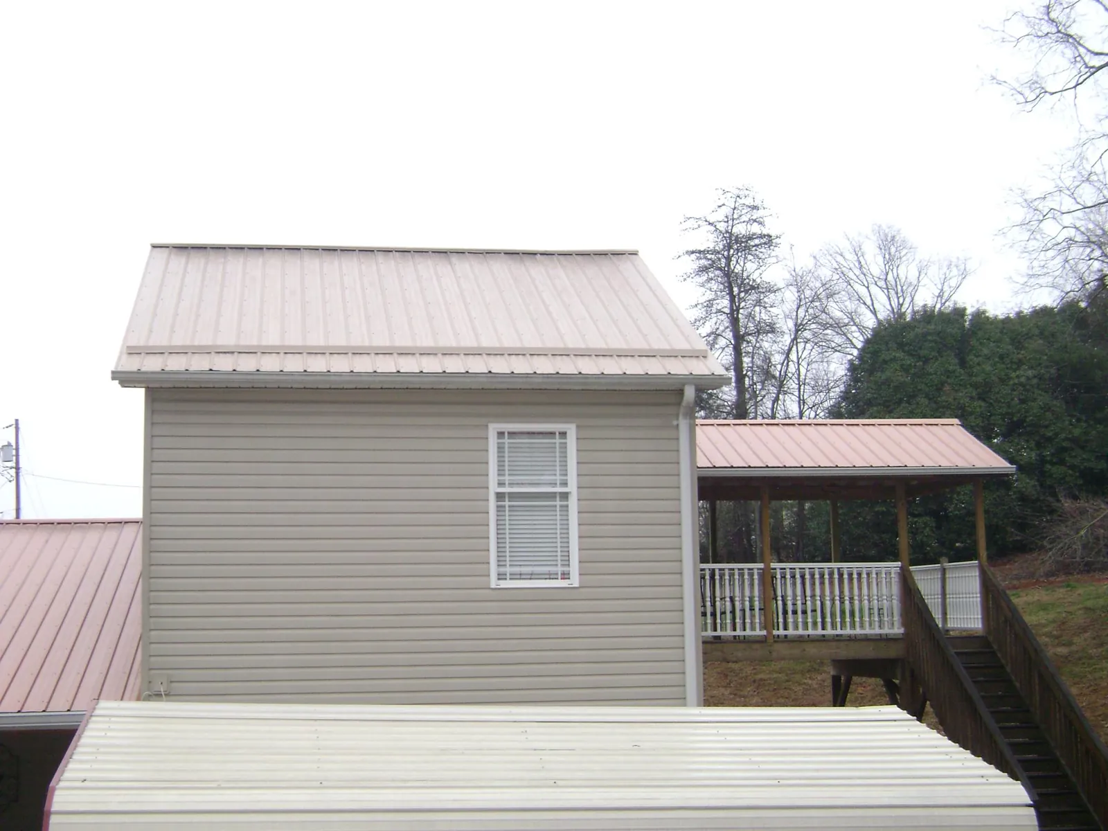 Tan metal roofs on a two story addition and attached porch, from a Roof Replacement job in Weston